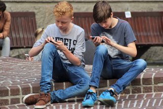 Zwei Jungs sitzen auf dem Boden im Schulhof und schauen in ihre Smartphones.
